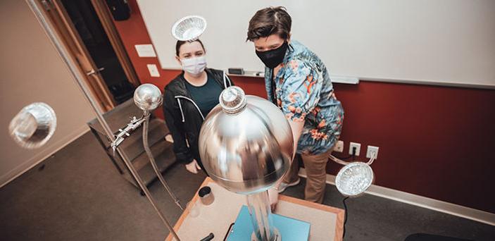 2 BSU students operating an electro magnetic tower with small foil pie plates on the top 和 flying in the air around it